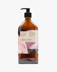 A recycled amber glass pump bottle of Roseum Conditioner with a label featuring 'Flamingos' artwork by Meinke Flessemen and the text 'roséum' part of the rose geranium botanical, Pelargonium roseum.