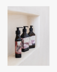 Lifestyle: three pump bottles of Roseum Shampoo and Conditioner with a labels featuring 'Flamingos' artwork by Meinke Flessemen and the text 'roséum' part of the rose geranium botanical, Pelargonium roseum.