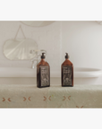 La Eva x Petersham Nurseries Blu face and body wash on a embroidered towel in front of a bath
