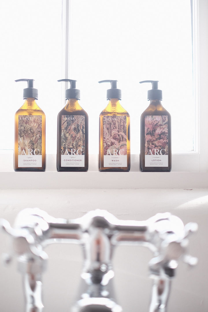 collection of four amber recycled glass bottles on a bathroom window ledge with bespoke dual branded labels featuring La-EVA and ARC for Spice shampoo and conditioner and Roseum wash and lotion La-Eva