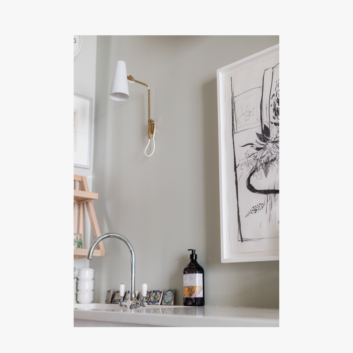 Lifestyle: A recycled amber glass pump bottle of Phos Hand & Body Wash with a label featuring artwork by Emma Cassi, on a beautiful bathroom sink Phos; lemongrass, May Chang and basil
