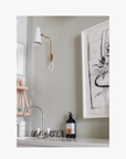 Lifestyle: A recycled amber glass pump bottle of Phos Hand & Body Wash with a label featuring artwork by Emma Cassi, on a beautiful bathroom sink Phos; lemongrass, May Chang and basil
