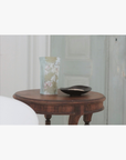 Lifestyle: A standing pouch of La-Eva Linden salts with Valeska Hykel artwork label sits on a round wooden table beside a small black dish in a softly lit interior setting