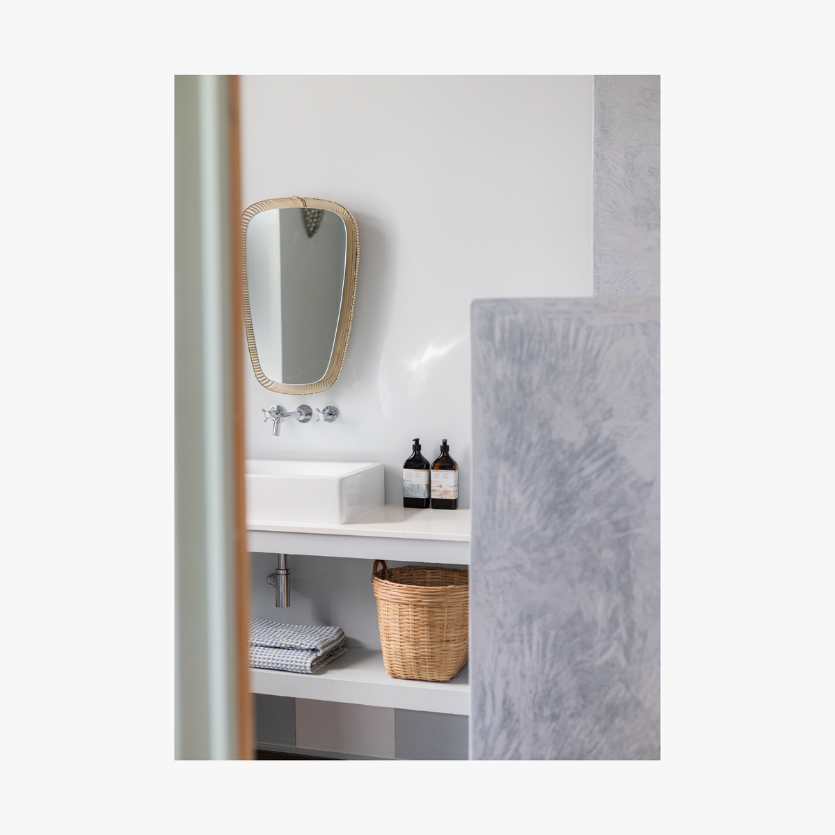 Bathroom shelf with bottles of the La-Eva refillable amenities spice collection and a vase against a light grey wall. Featuring artwork by Emma Cassi