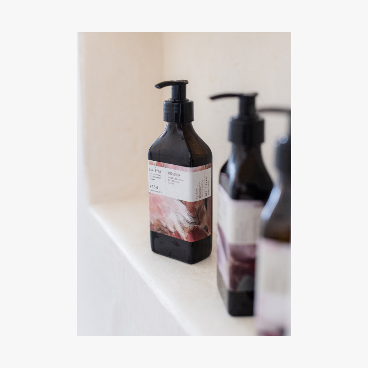 Two pump bottles of Roseum Hand & Body Wash with a label featuring 'Flamingos' artwork by Meinke Flessemen and the text 'roséum' part of the rose geranium botanical, Pelargonium roseum.