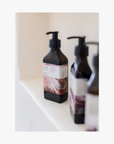 Two pump bottles of Roseum Hand & Body Wash with a label featuring 'Flamingos' artwork by Meinke Flessemen and the text 'roséum' part of the rose geranium botanical, Pelargonium roseum.