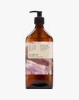 A recycled amber glass pump bottle of Roseum Shampoo with a label featuring 'Flamingos' artwork by Meinke Flessemen and the text 'roséum' part of the rose geranium botanical, Pelargonium roseum.