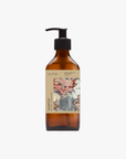 A recycled amber glass pump bottle of La-eva Roseum Shampoo with a label featuring 'Younger Together' artwork by Valeska Hykel and the text 'roséum ', part of the rose geranium botanical, Pelargonium roseum.