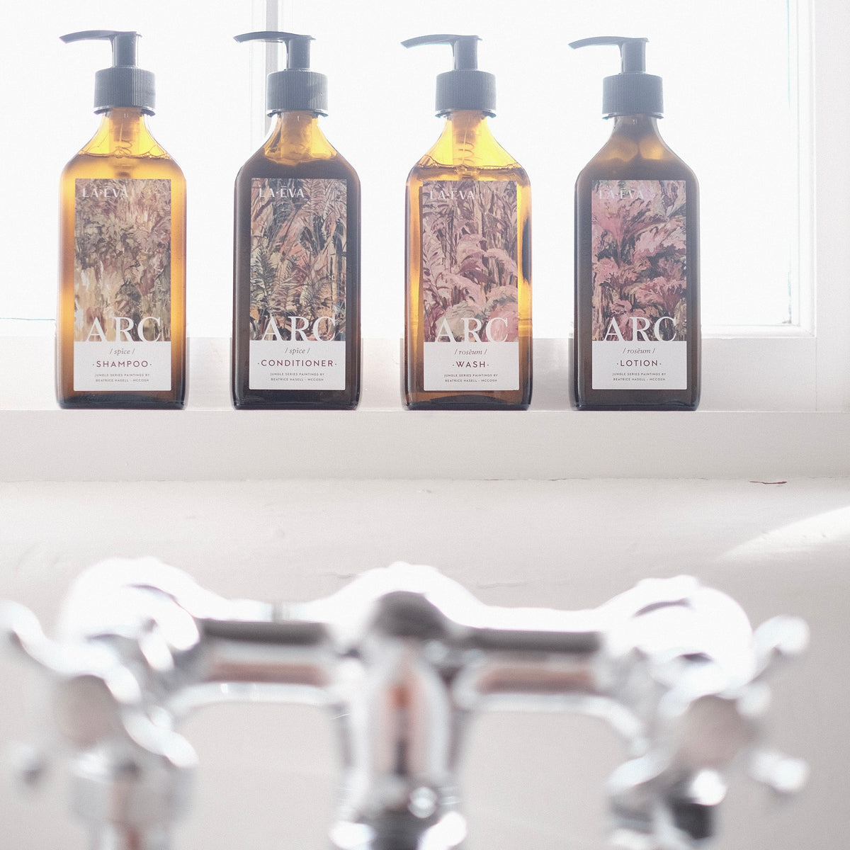 Lifestyle: Four recycled amber glass pump bottles of Roseum Hand & Body Wash, Lotion, Shampoo and Conditioner with bespoke artwork for ARC architecture by artist Beatrice Hassel McCosh. 