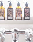 Lifestyle: Four recycled amber glass pump bottles of Roseum Hand & Body Wash, Lotion, Shampoo and Conditioner with bespoke artwork for ARC architecture by artist Beatrice Hassel McCosh. 