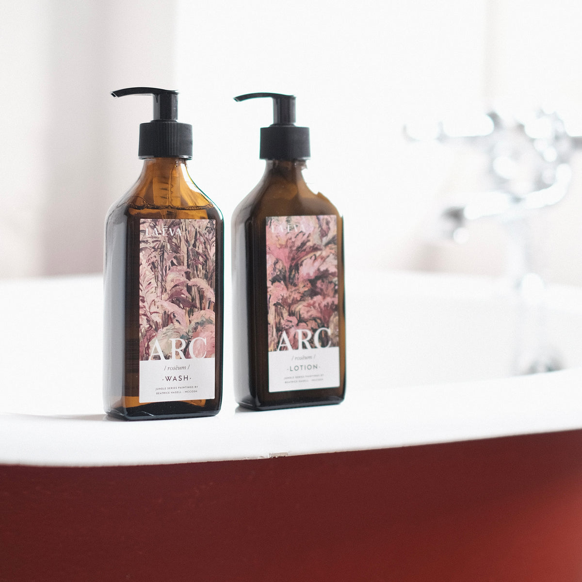 Lifestyle: Two recycled amber glass pump bottles of Roseum Hand & Body Wash and Lotion with bespoke artwork for ARC architecture by artist Beatrice Hassel McCosh. 