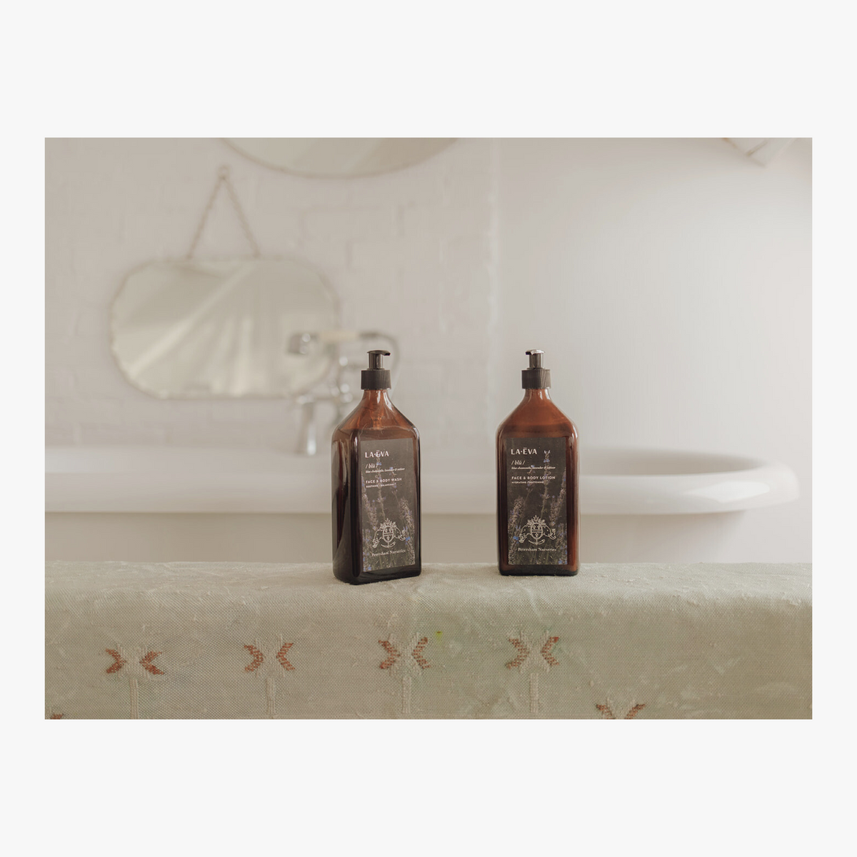 La Eva x Petersham Nurseries Blu face and body wash on a embroidered towel in front of a bath