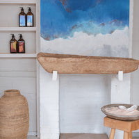 Scene from the La-Eva studio showing a display shelf with six 500ml glass bottles featuring special edition labels with the art of Nathalie Moisy, and a blue painting by Nathalie Moisy