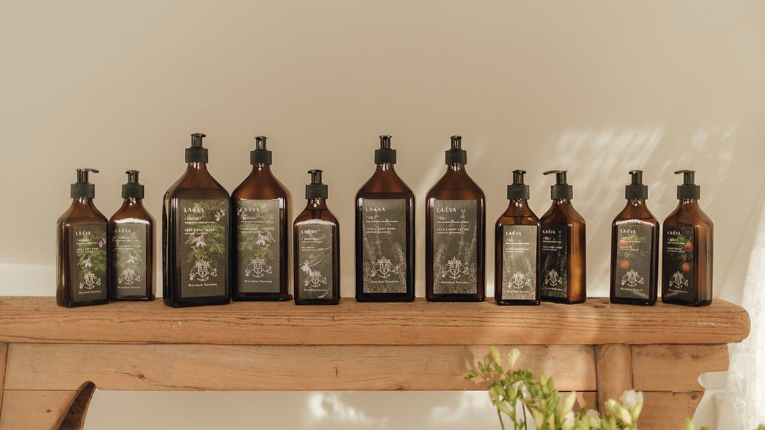 Full collection of La-Eva products in 200ml and 500ml glass bottles featuring special edition Petersham Nurseries labels displayed on a wooden bench