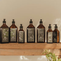 Full collection of La-Eva products in 200ml and 500ml glass bottles featuring special edition Petersham Nurseries labels displayed on a wooden bench